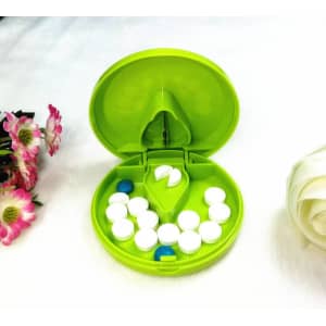 A green plastic pill cutter and pill box, containing white and blue pills, with floral decorations nearby.