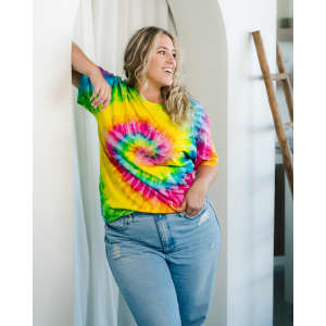 A vibrant tie-dye adult T-shirt featuring a swirl of yellow, pink, blue, and green colours, paired with light blue jeans.