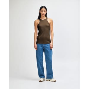 A woman wearing an olive green racerneck tank top and loose blue cargo jeans, standing with a relaxed pose.