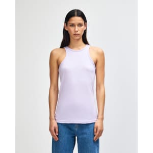 A women's racerneck tank in lavender, featuring a fitted silhouette and a logo. The model is wearing loose-fitting jeans.