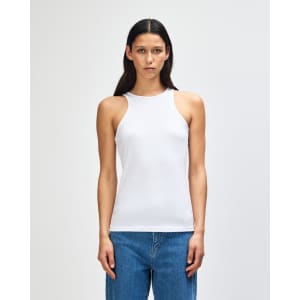 A white women's racerneck tank top with a fitted design, displayed on a model. It features a branding logo.