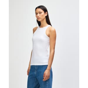 A woman in a white racerneck tank top stands sideways, showcasing the fit. The top has a subtle design and a brand logo.