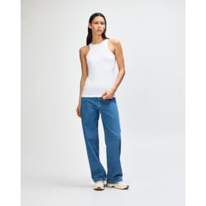 A white women's racerneck tank top worn with light blue wide-leg jeans, featuring a logo on the tank.