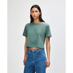 A model wearing a green boxy t-shirt, with short sleeves and loose fit, paired with light denim jeans.