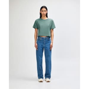 A model wears a green boxy t-shirt with light blue cargo jeans and sneakers, featuring a casual style.