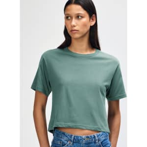 A woman wearing a teal boxy t-shirt, styled with light blue denim shorts. The shirt has a logo.