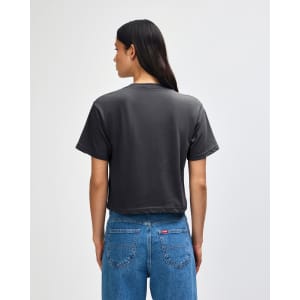 A grey boxy t-shirt is worn by a person with curly hair, standing with their back to the camera.
