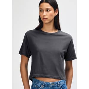 A woman models a grey boxy T-shirt with short sleeves and a relaxed fit, paired with light denim jeans.