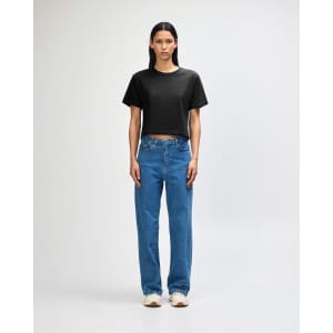 A woman wearing a black boxy T-shirt and wide-leg blue jeans, standing against a white background.