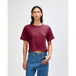 A boxy maroon T-shirt is displayed on a model, paired with light blue jeans. The shirt has a logo.