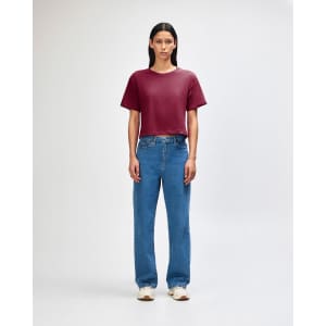 A woman stands wearing a burgundy boxy T-shirt and light blue cargo jeans, paired with black and white sneakers.