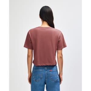 A woman with curly hair wearing a dusty rose boxy t-shirt, viewed from the back, with light blue cargo pants.