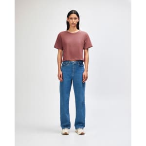 A woman's boxy t-shirt in rose, paired with light blue cargo jeans, featuring a logo on the shirt.