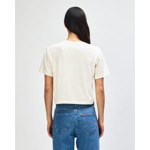 A beige women's boxy t-shirt with short sleeves, viewed from the back, featuring a logo. Casual style, perfect for layering.