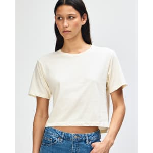 A light cream women's boxy t-shirt displayed on a model, featuring a logo on the garment.