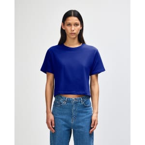 A blue women's boxy T-shirt with short sleeves, featuring a logo on the fabric, styled with light jeans.