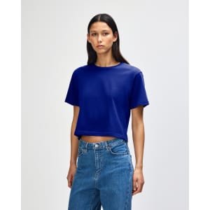 A blue boxy T-shirt with short sleeves, displayed on a model wearing jeans. The shirt has a logo.