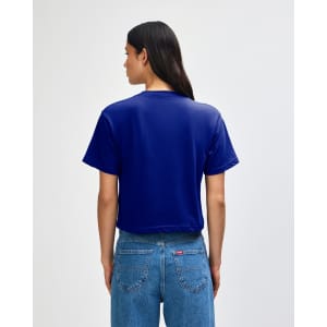A blue boxy t-shirt with short sleeves and a back view. The model wears high-waisted jeans and has curly hair.