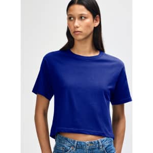 A woman wearing a blue boxy t-shirt, styled with denim shorts, featuring a branded logo.
