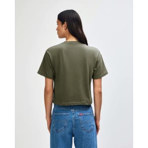 A back view of a women's olive green boxy T-shirt, paired with light blue cargo jeans. Features a logo.