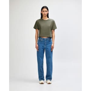 A woman stands wearing an olive green boxy t-shirt and light blue cargo jeans, paired with black and white sneakers.