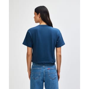 A navy blue women's boxy T-shirt featuring a loose fit, viewed from the back. The model wears light blue cargo pants.