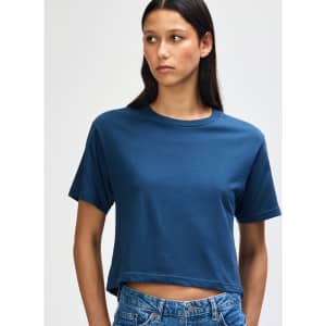 A navy blue boxy t-shirt with short sleeves, displayed on a model with curly hair. The shirt has a logo.