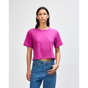 A vibrant fuchsia women's boxy T-shirt with a relaxed fit, paired with light blue jeans. Features a branding logo.