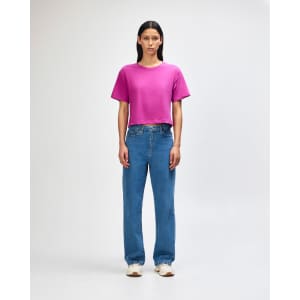 A boxy women's T-shirt in vibrant magenta, paired with light blue wide-leg jeans. The model stands with hands on hips.
