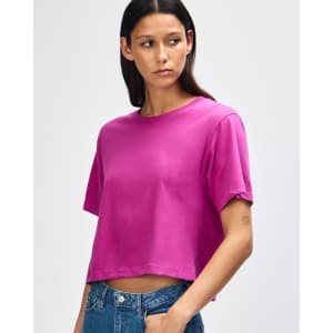 A woman wearing a bright pink boxy t-shirt, featuring a crew neck and short sleeves. The shirt has a logo.