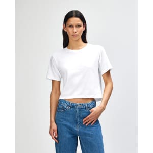 A white boxy T-shirt featuring short sleeves, paired with blue jeans, and has a logo on it.