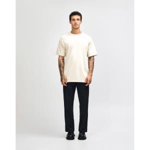A model wearing a lightweight off-white unisex t-shirt paired with blue jeans and white sneakers, featuring a logo.