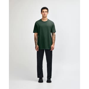 A person wearing a dark green heavyweight cotton unisex T-shirt and light blue cargo pants, standing with hands behind.