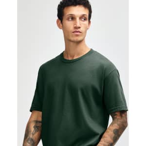A heavyweight cotton unisex t-shirt in dark green, worn by a model with curly hair. Features a simple, classic design.