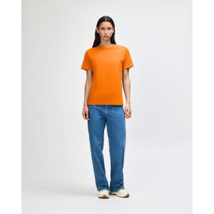A heavyweight unisex t-shirt in bright orange, paired with light blue baggy jeans, modeled by a young person.