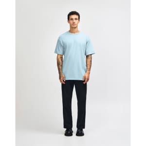 A light blue heavyweight cotton unisex T-shirt worn with baggy denim jeans, featuring a logo on the shirt.