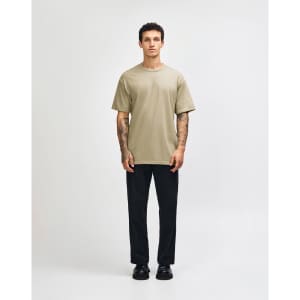 A unisex heavyweight cotton t-shirt in olive green, paired with light blue cargo jeans. The model has curly hair.