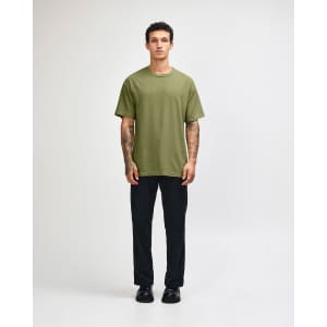 A green heavyweight cotton t-shirt worn by a model, paired with cargo pants and casual shoes, with a subtle logo.