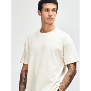 A unisex heavyweight cotton T-shirt in cream, featuring a relaxed fit and a subtle branding logo.