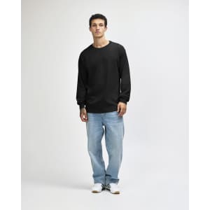A model wearing a black heavyweight cotton unisex long sleeve T-shirt, paired with green cargo pants and white sneakers.