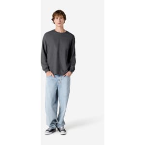 A heavyweight unisex long sleeve t-shirt in grey, paired with light blue jeans and black sneakers, displayed on a model.