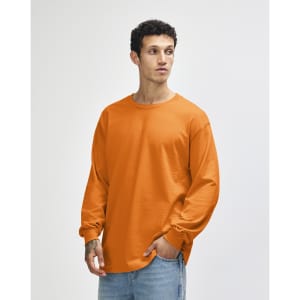 An orange heavyweight cotton unisex long sleeve t-shirt displayed on a model, featuring a simple design and sleeves with cuffed ends.