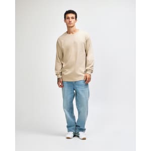 A lightweight long sleeve T-shirt in beige, paired with blue jeans, worn by a model in a casual pose.
