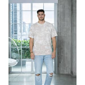 A man stands wearing a bleach-out dyed T-shirt in neutral tones, paired with ripped blue jeans.