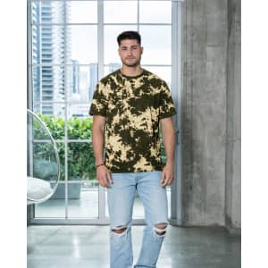 A man stands in a modern interior wearing a bleached tie-dye t-shirt in olive green and cream colours.