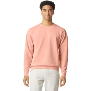 A lightweight crewneck sweatshirt in pastel pink featuring a logo. The model is wearing light-coloured pants.