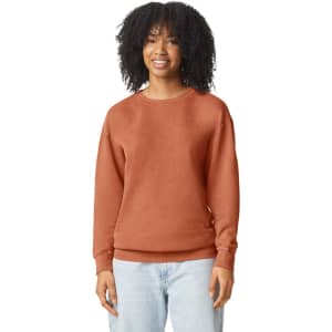 A woman wears an orange-brown lightweight crewneck sweatshirt, featuring a relaxed fit and long sleeves.