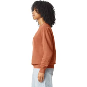 A lightweight crewneck sweatshirt in a warm rust colour, featuring a side view of a model with curly hair.