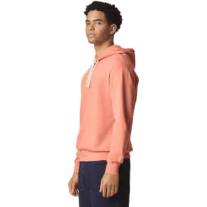 A lightweight hooded sweatshirt in coral with a drawstring hood, showcased on a model from the side.