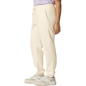 Lightweight cream sweatpants with pockets, featuring a drawstring waist and a logo. Model wears them with sneakers.